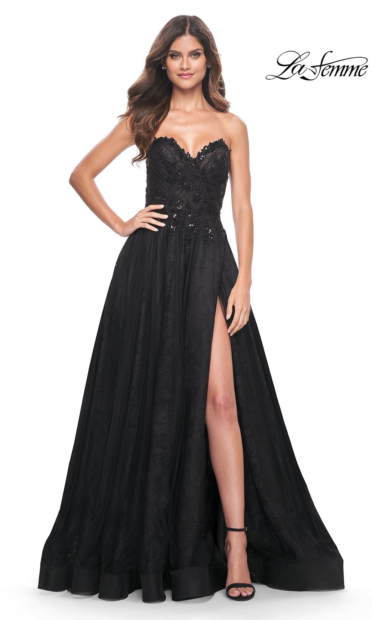 A woman stands against a white background wearing the La Femme Strapless Long Prom Ball Gown 31954, featuring a sweetheart neckline, black evening silhouette, floral embellishments, and a high slit.